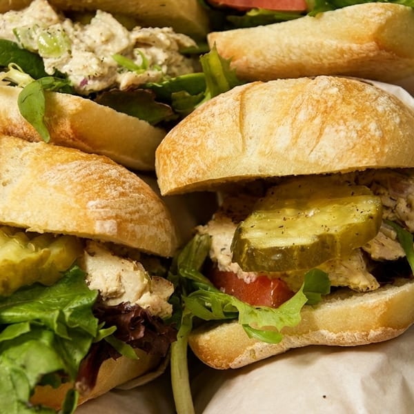 Several chicken salad sandwiches on ciabatta rolls with lettuce, tomato, and pickles.