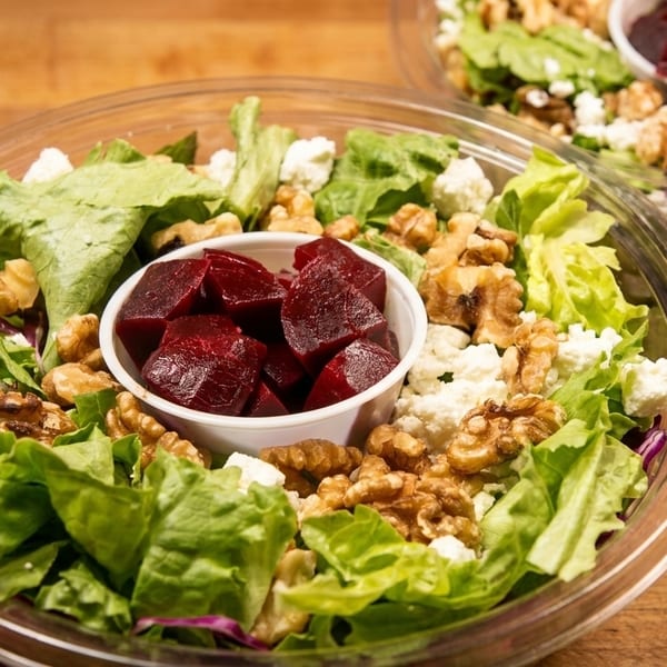 Two plastic containers of fresh green salad with walnuts, feta cheese, and a cup of beets.